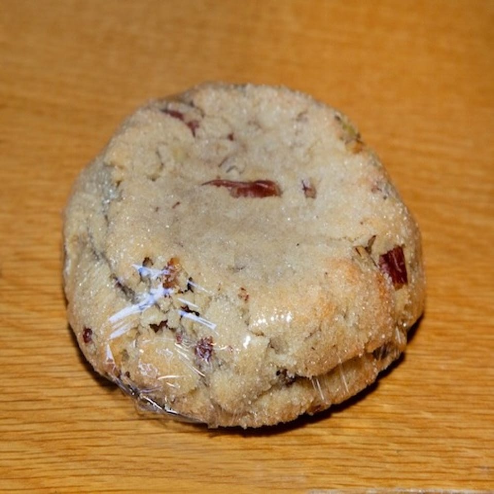 Round crumbly cookie studded with dried red fruit, wrapped in plastic and resting on a wooden surface.