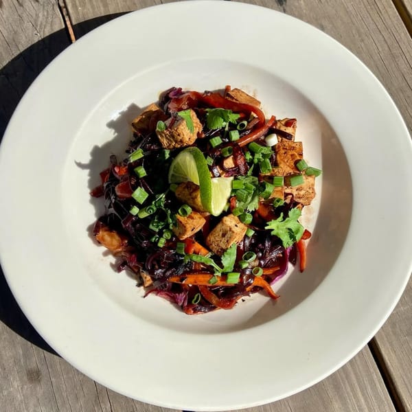 Vegan stir-fry with tofu, red cabbage, carrots, and scallions, garnished with lime and cilantro.