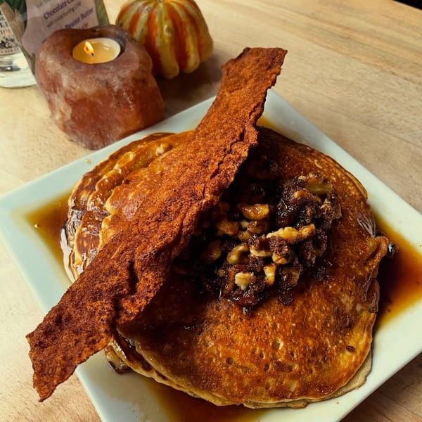 Vegan pancakes with syrup, walnuts, and a crispy bacon substitute, next to a candle and gourd.