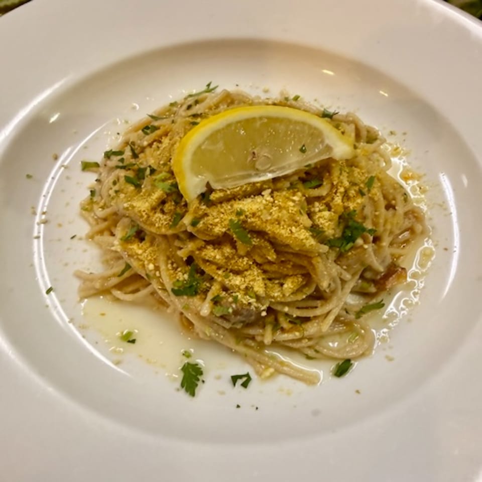 Plate of spaghetti topped with golden tofu pieces, herbs, breadcrumbs, and a lemon slice.