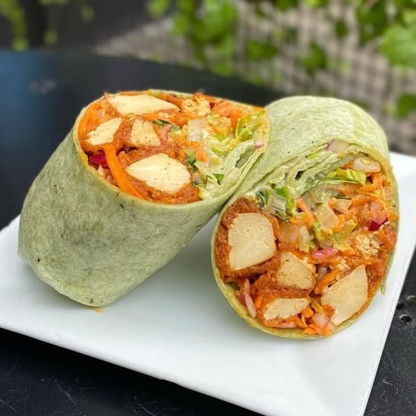 Two halves of a vegan buffalo chicken wrap, filled with plant-based chicken, lettuce, and carrots.