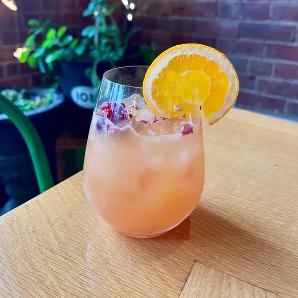 A vegan cocktail with an orange slice and rose petals on a wooden table at ION Restaurant.