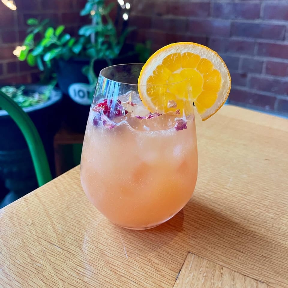 A vegan cocktail with an orange slice and rose petals on a wooden table at ION Restaurant.