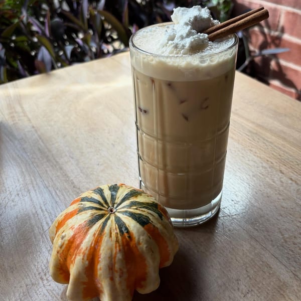 Vegan iced latte with whipped cream and cinnamon sticks, next to a decorative gourd on a wooden table.