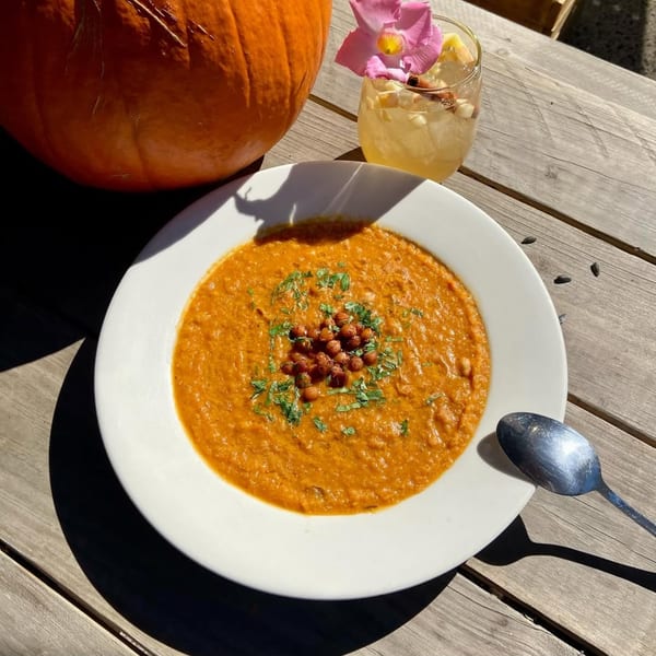 Vegan pumpkin soup with chickpeas and cilantro, a cocktail, and a pumpkin on a wooden table.