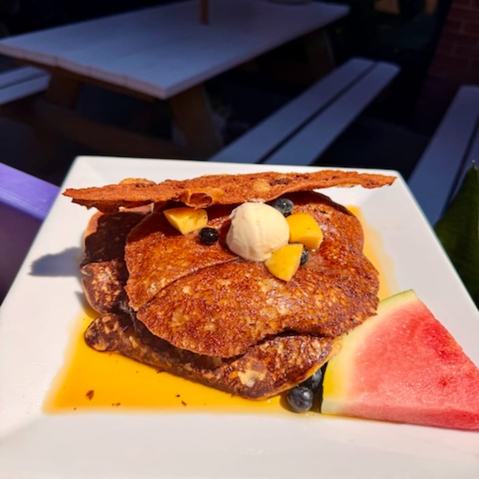 Stacked chocolate pancakes topped with vanilla ice cream, mango pieces, blueberries, and crisp chocolate garnish on a white plate.