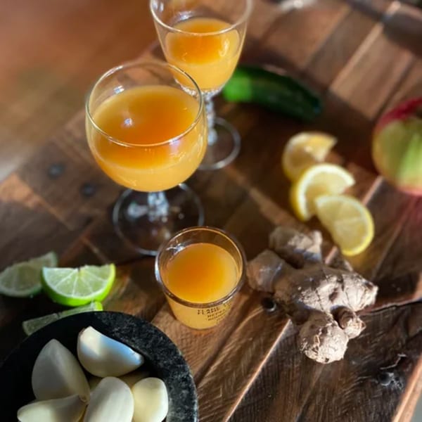 Three glasses of orange juice, garlic cloves, ginger, lime, and lemon slices on a wooden board.